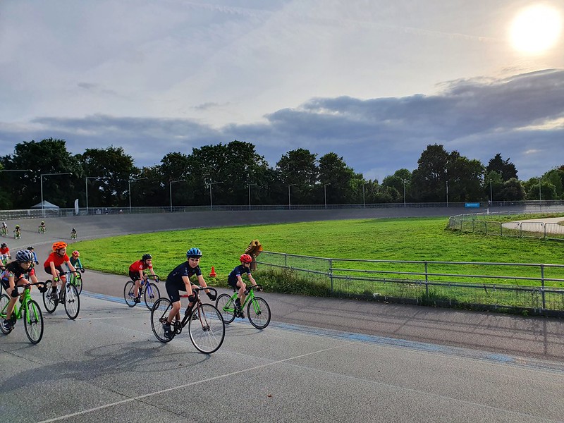 Alex riding at the front of a small peloton of riders on a velodrome track.