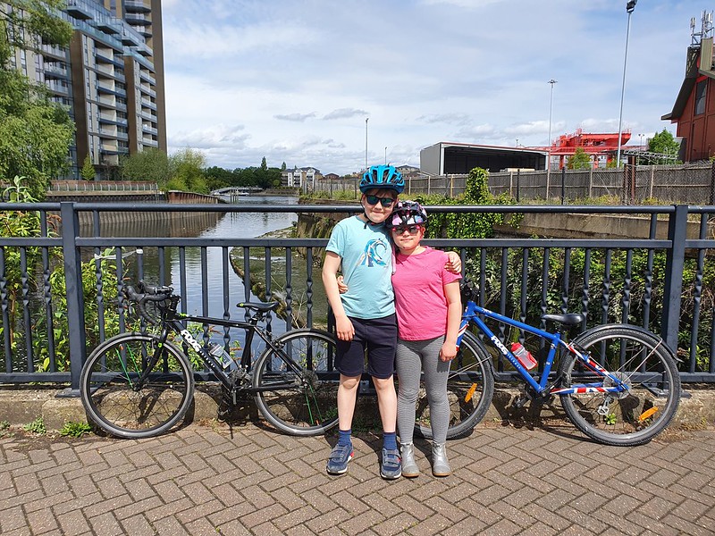 Alex and Sophie hugging each other in front of their bikes by the River Thames.
