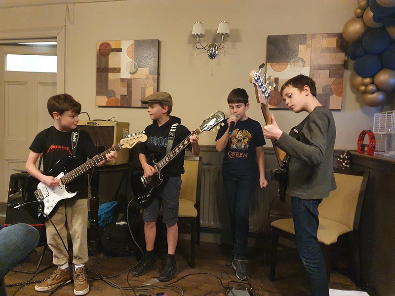 Alex singing in his rock band alongside two guitarists and a bass guitarist